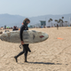 A masked surfer walking at Venice Beach in California during Memorial Day weekend in May.